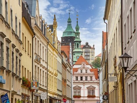 Narrow street in Pirna with colorful historic buildings leading to a church with green copper spires under blue sky.