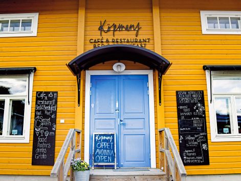 Ein Cafe in einem gelben landestypischen Holzhaus mit blauer Eingangstür