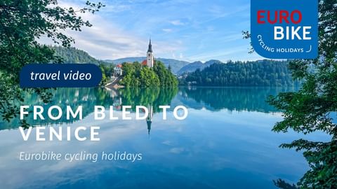 Lake Bled in Slovenia with a small island featuring a church with a tall spire, surrounded by forested mountains and reflected in calm water.
