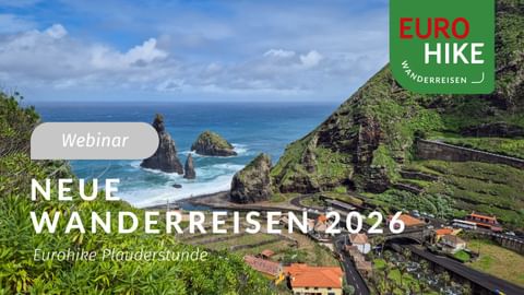 Dramatische Küstenlandschaft mit grünen Klippen, Felsformationen im blauen Meer und kleinem Dorf mit roten Dächern entlang einer Straße.