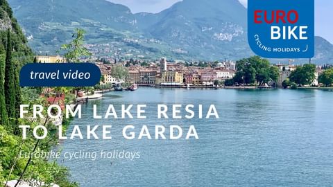 Lakeside town with historic buildings and mountains. Text overlay: 'From Lake Resia to Lake Garda' with Eurobike cycling holidays logo.