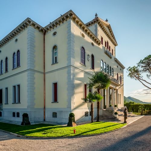 Elegante neoklassizistische Villa Soligo in Farra di Soligo mit cremefarbener Fassade, Ziergesimsen und Bogenfenstern. Palmen und gepflegter Rasen davor.