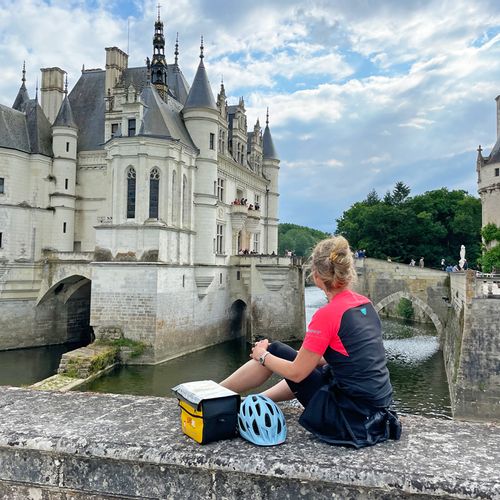 Radlerin sitzt auf Mauer vor Schloss Chenonceau