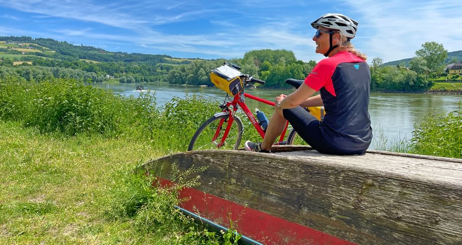 Radlerin bei der Pause sitzend auf einem umgedrehten Boot am Ufer der Donau