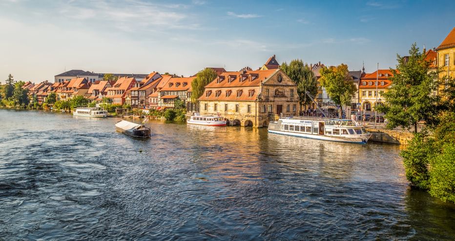 Historic waterfront of Bamberg's Little Venice with colorful half-timbered houses along the Regnitz River and tourist boats docked at the shore.