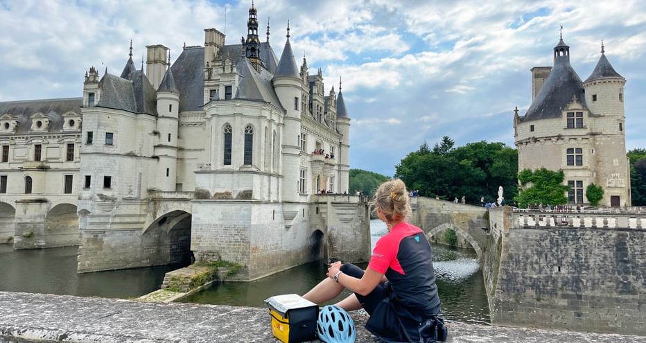 Eine Radfahrerin sitzt auf einer Steinmauer vor dem Schloss Chenonceau an der Loire