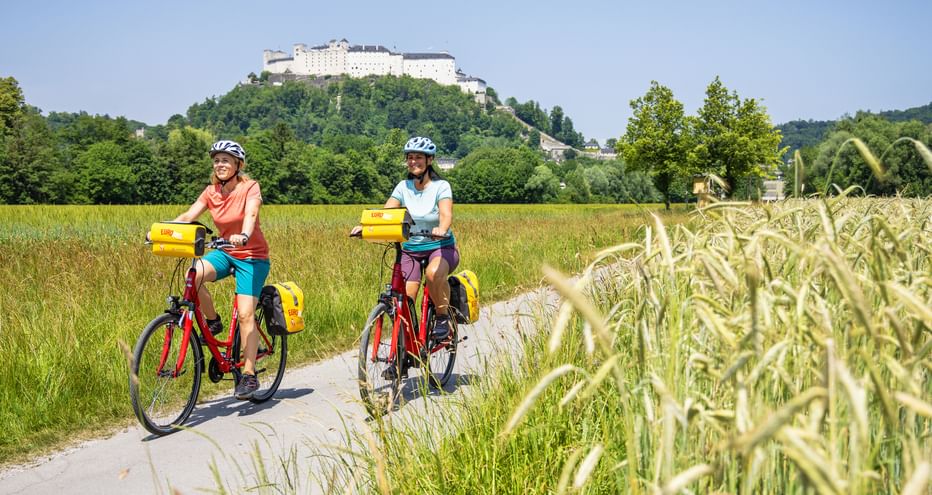 Zwei Radfaherinnen auf der Hellbrunner Allee in Salzburg, im Hintergrund die Festung