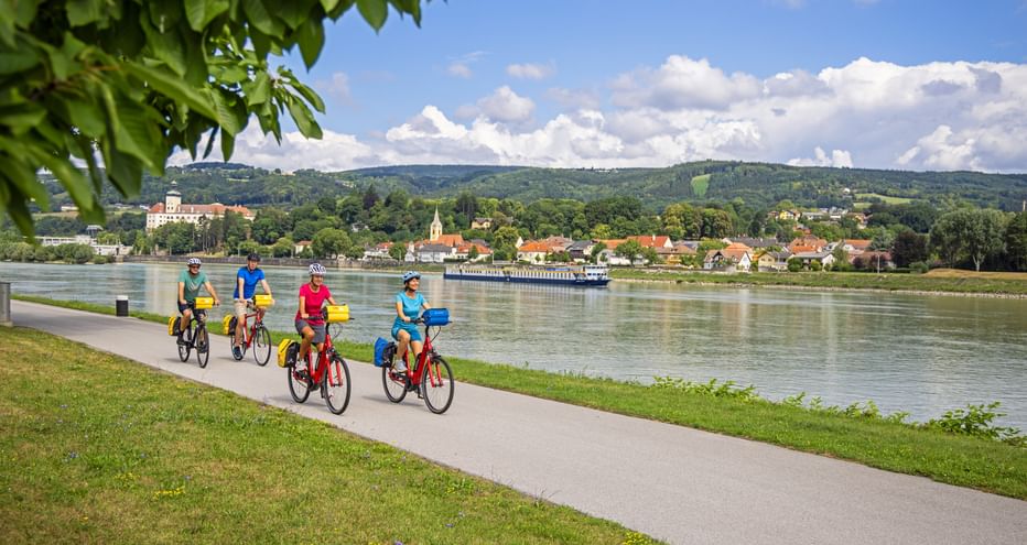 A cycling group rides along the banks of the Danube, with the village of Persenbeug in the background