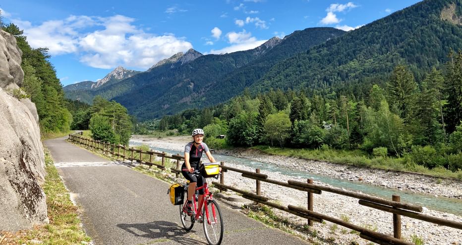 Radfahrerin entlang des Flussen, mit Bergpanorama im Hintergrund
