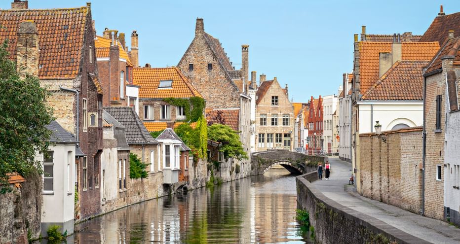 Malerischer Kanal in Brügge, gesäumt von mittelalterlichen Backsteinhäusern mit orangen Ziegeldächern. Eine Steinbrücke überquert das ruhige Wasser.