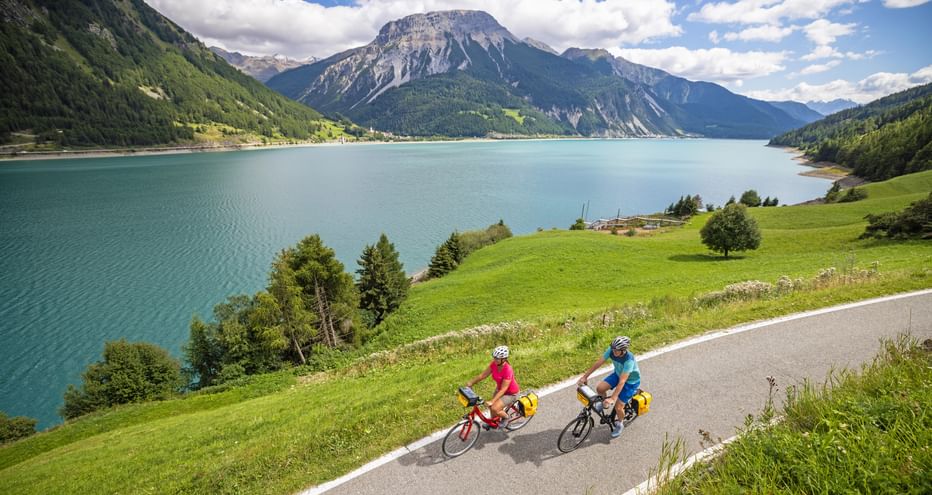 Two cyclists on well-maintained cycle paths at Lake Resia with mountain panorama in the background