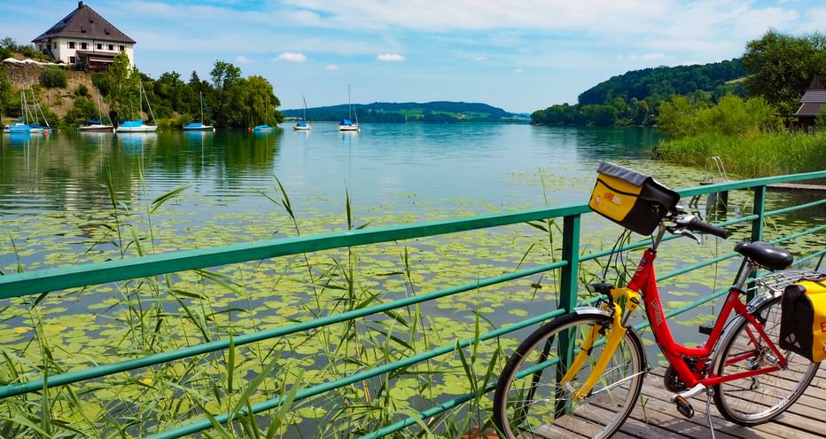 A bicycle stands on a footbridge in Weyerbucht in Mattsee with a view of Schlossberg mountain