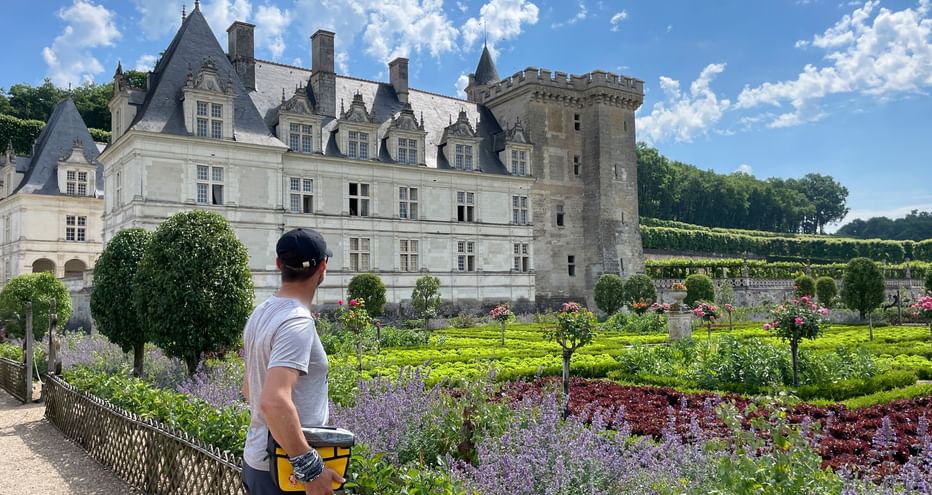 Radfahrer mit Helm betrachtet Schloss Villandry und seine Ziergärten mit bunten Blumenbeeten, geschnittenen Hecken und blauem Himmel.