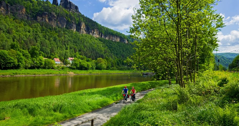 Two cyclists riding along the Elbe, rocks and forests in the background