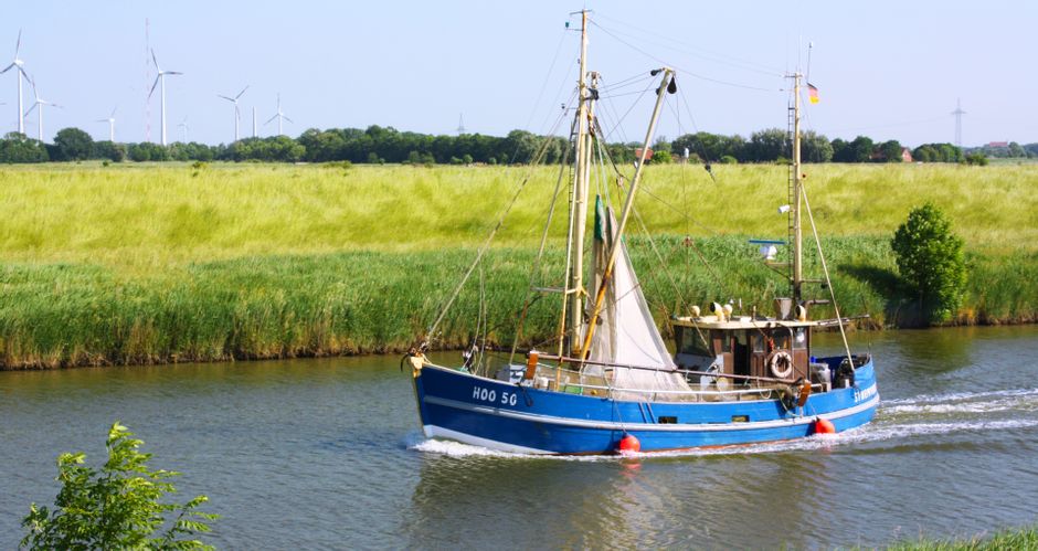 A small fishing boat on a small river surrounded by fields, wind turbines in the background
