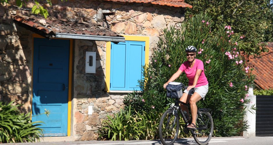 Radfahrerin vor einem landestypischen Steinhaus mit bunten Fenstern und Türen
