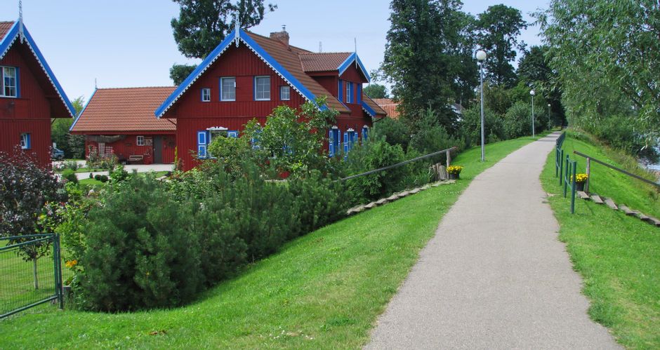 Rote Häuser mit blauen Fensterläden und Giebeln neben einem Radweg des Dorfes Rusne