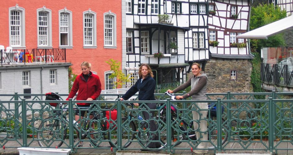 Drei Radfahrerinnen auf einer Brücke in der Altstadt mit Fachwerkhäusern