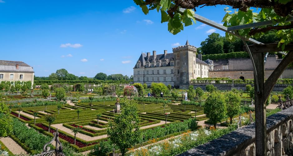 Château de Villandry with formal French gardens featuring geometric hedges, topiary trees, and ornamental patterns under a blue sky.