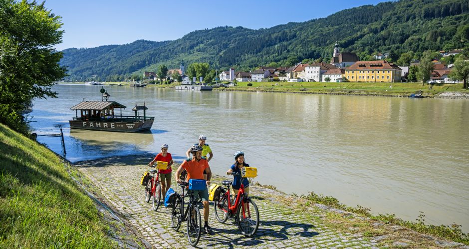 Cycling group leaving the bicycle ferry, in the background the departing ferry and the village of Engelhartszell.