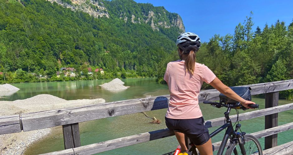 Radfahrerin bei der Pause auf der Draubrücke im Rosental, im Hintergrund bewaldete Berge