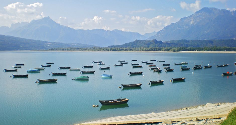 Panoramic view of Lago di Santa Croce with many small boats in the foreground and mountains in the background