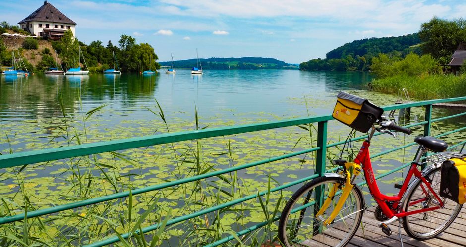 Ein Fahrrad steht auf einem Steg in der Weyerbucht in Mattsee mit Blick auf den Schlossberg
